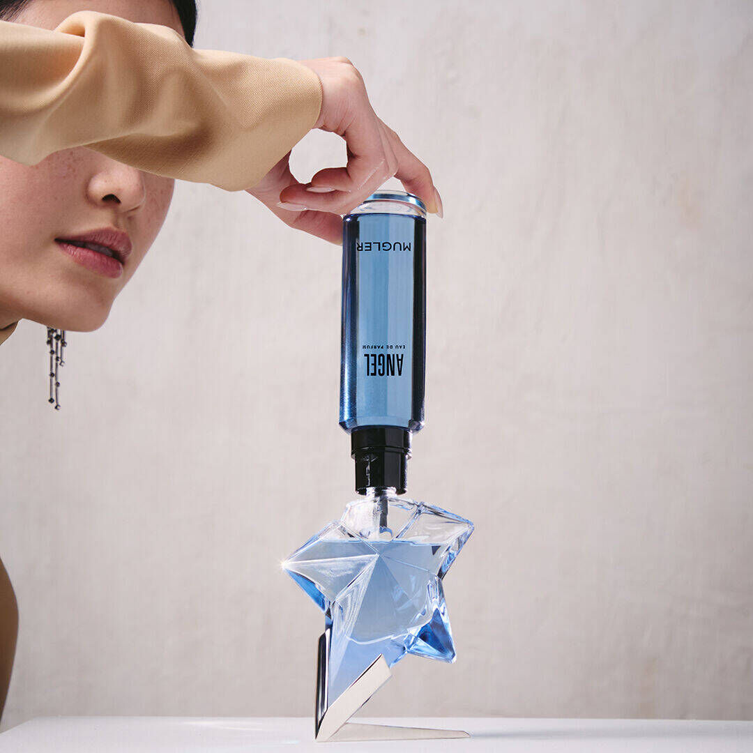 un flacon de parfum bleu angel qui est rempli par une recharge tenue dans une main