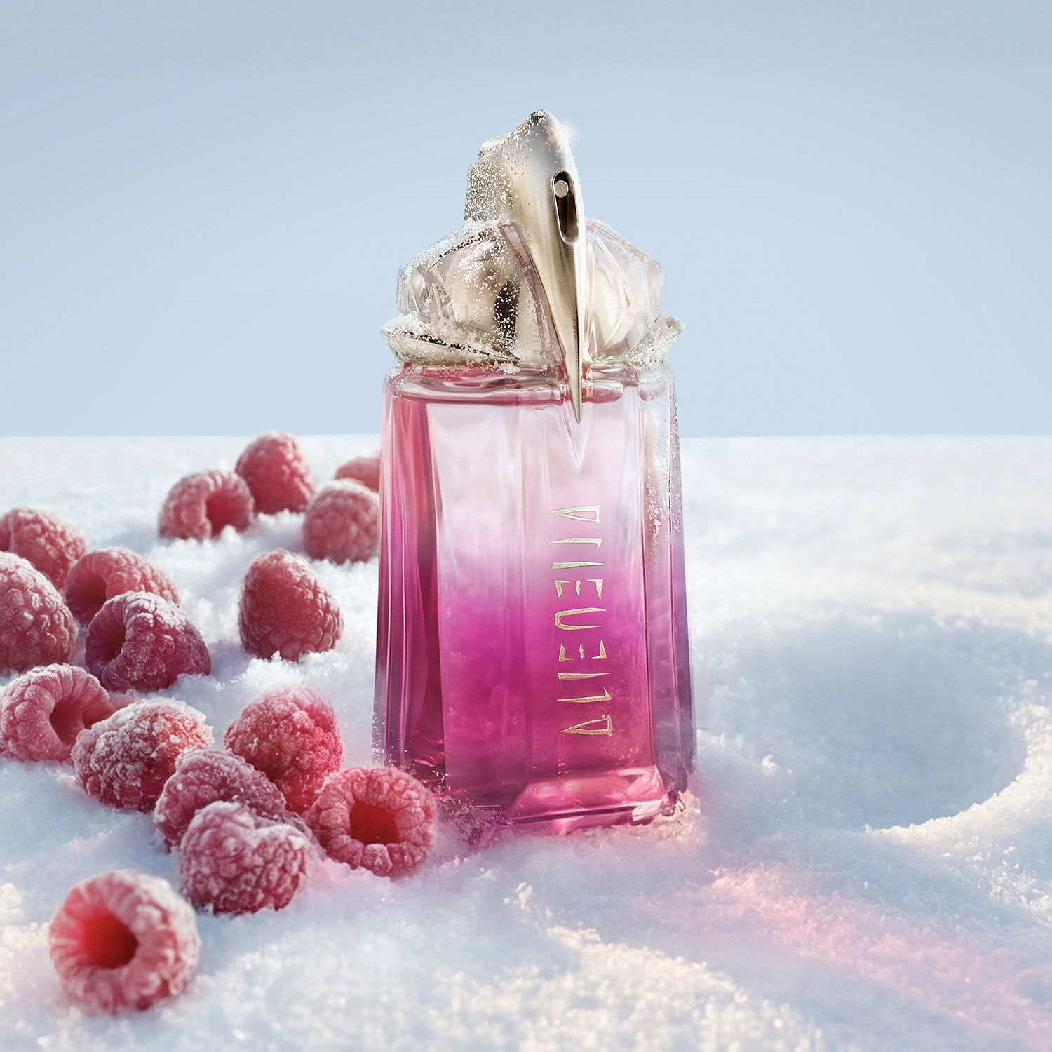 Un flacon de parfum Mugler rose vif Alien pulp eau de parfum dresse dans la neige, avec plusieurs framboises rouges fraiches eparpillees autour de sa base.