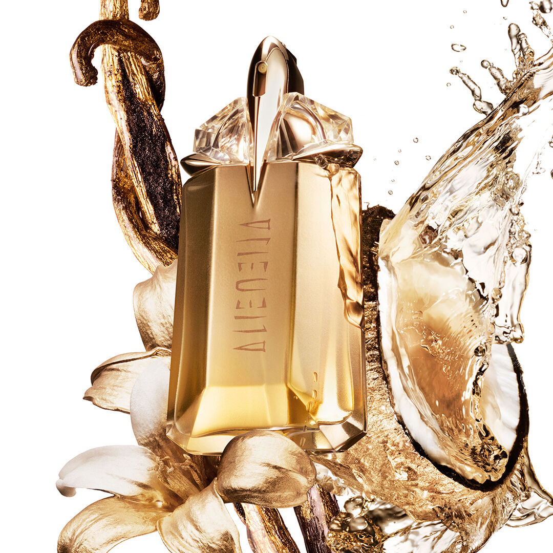 un flacon de parfum dore mugler entoure d'une noix de coco, d'une fleur de jasmin et de morceau de vanille