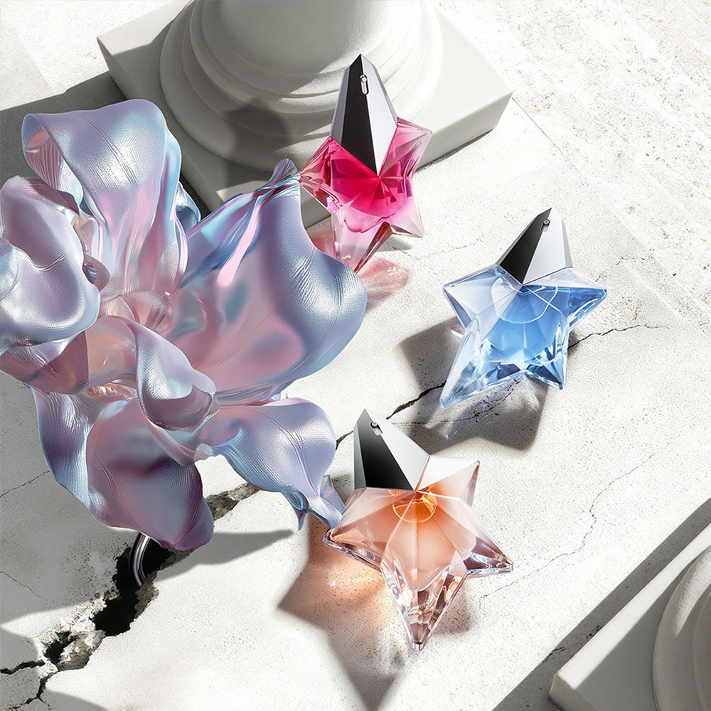 Banniere de campagne Mugler pour la fete des meres 2026, presentant les emblematiques bouteilles de parfum de la franchise Angel dans un paysage celeste floral et parisien, celebrant des meres extraordinaires.