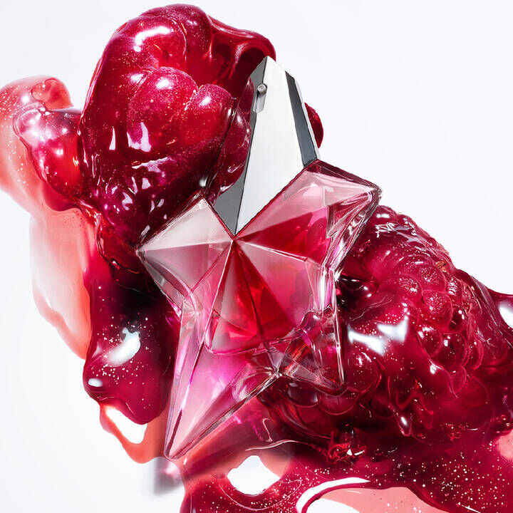 un flacon de parfum rose en forme d'etoile entoure de framboises rouges