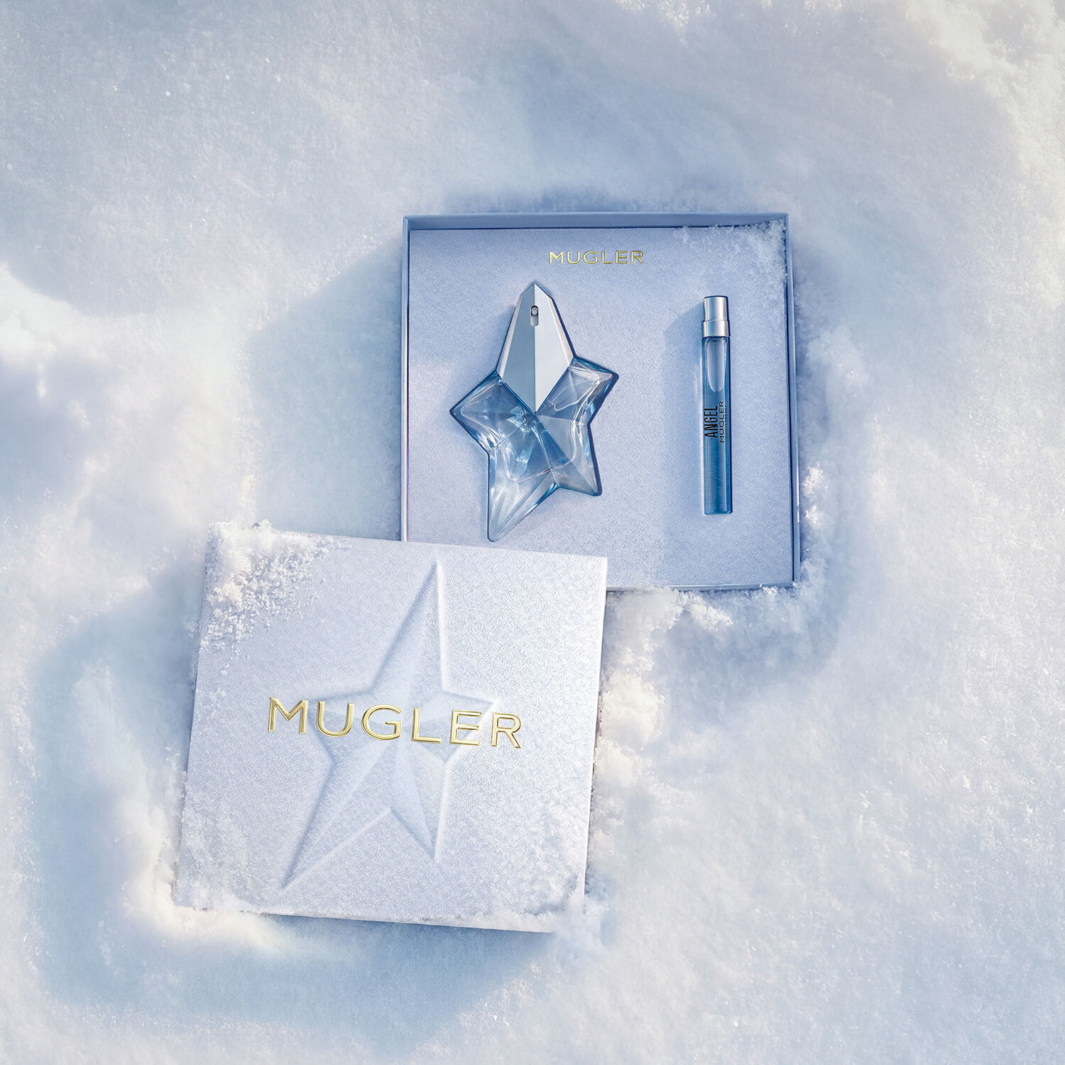 Un coffret cadeau Mugler ouvert, texture et bleu glace brillant, reposant sur la neige, revelant un coffret cadeau de 25 ml angel eau de parfum