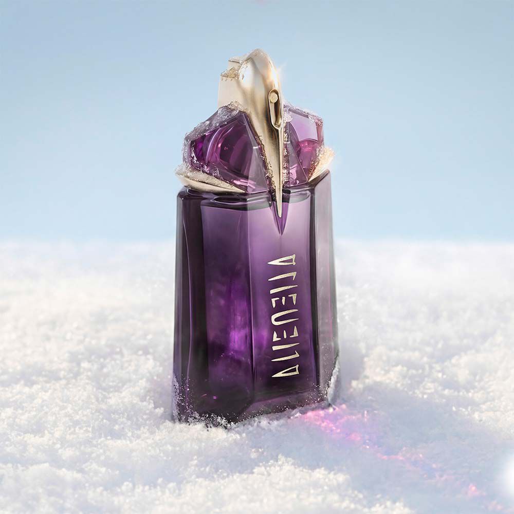 Le flacon signature de parfum Mugler, d’un violet profond, semblable a un talisman, Alien eau de parfum, debout dans une douce congere de neige blanche sous une lumiere vive et propre.