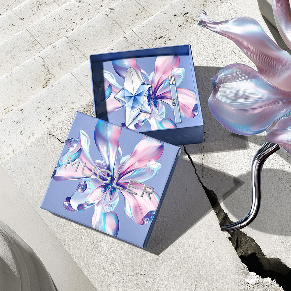 La boite cadeau de la fete des meres Mugler 2026 s’est ouverte pour reveler le duo Angel Eau de Parfum 50 ml et un spray de voyage, presente sur une surface en pierre ensoleillee avec une fissure en beton.