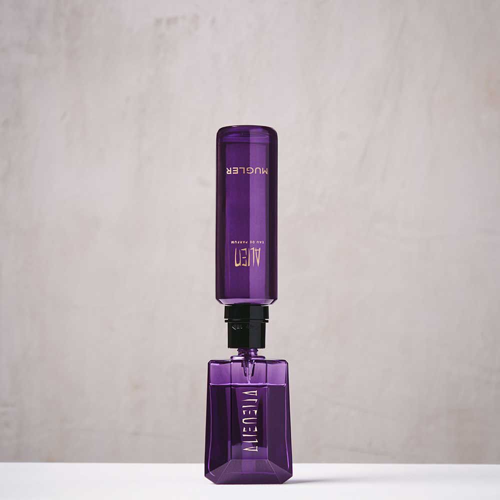 un flacon de parfum violet remplit par une recharge violet sur un fond beige