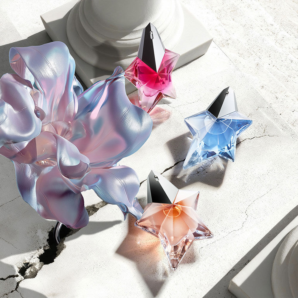Banniere de campagne Mugler pour la fete des meres 2026, presentant les emblematiques bouteilles de parfum de la franchise Angel dans un paysage celeste floral et parisien, celebrant des meres extraordinaires.