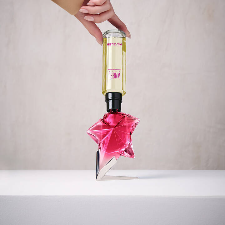 un flacon de parfum rose en forme d'etoile remplit par une recharge jaune tenue dans une main