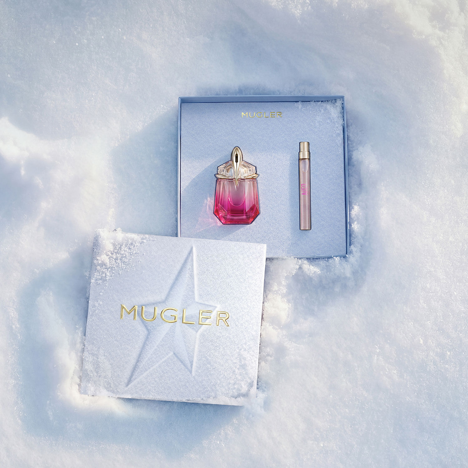 Un coffret cadeau Mugler ouvert, texture et bleu glace brillant, reposant sur la neige, revelant un coffret cadeau de 30 ml d’eau de parfum alien pulp