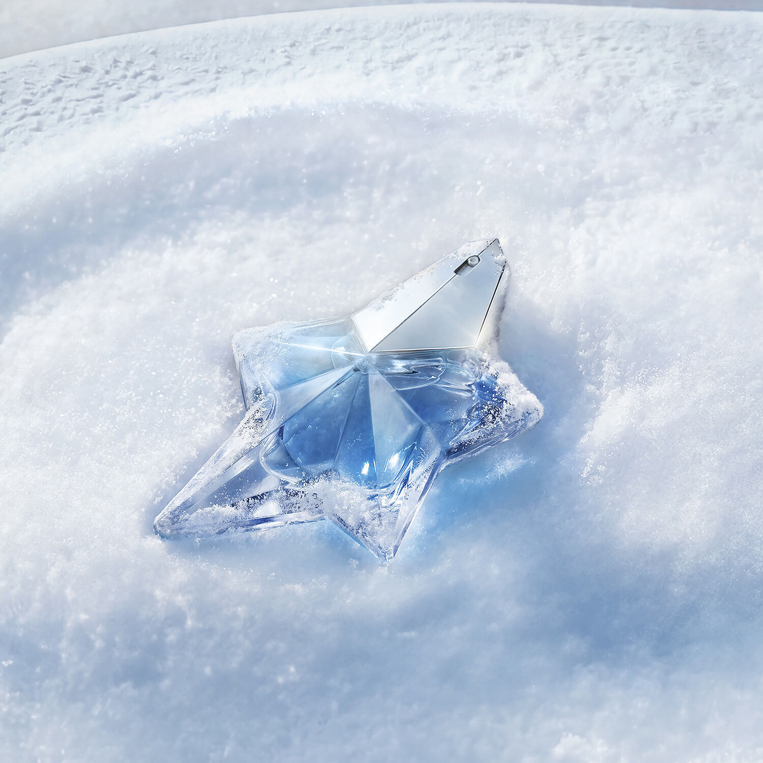 Un gros plan de la celebre bouteille de parfum Angel Mugler en forme d’etoile, bleu clair, en forme d’etoile, reposant elegamment sur un lit de neige blanche immaculee et etincelante sous une lumiere bleue douce.