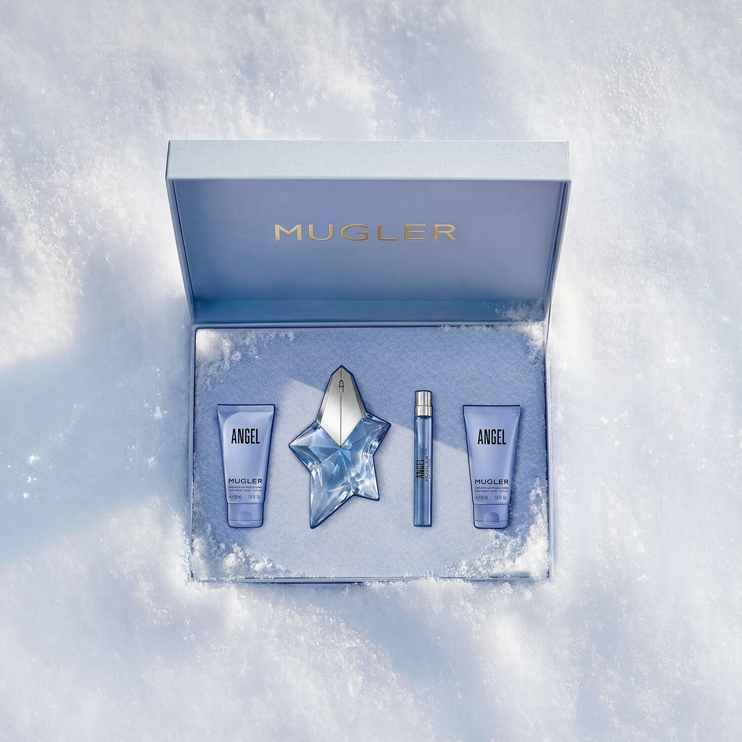 Un coffret Mugler ouvert, texture et bleu glace brillant, reposant sur la neige, revelant un coffret de luxe de 50 ml d’eau de parfum angel