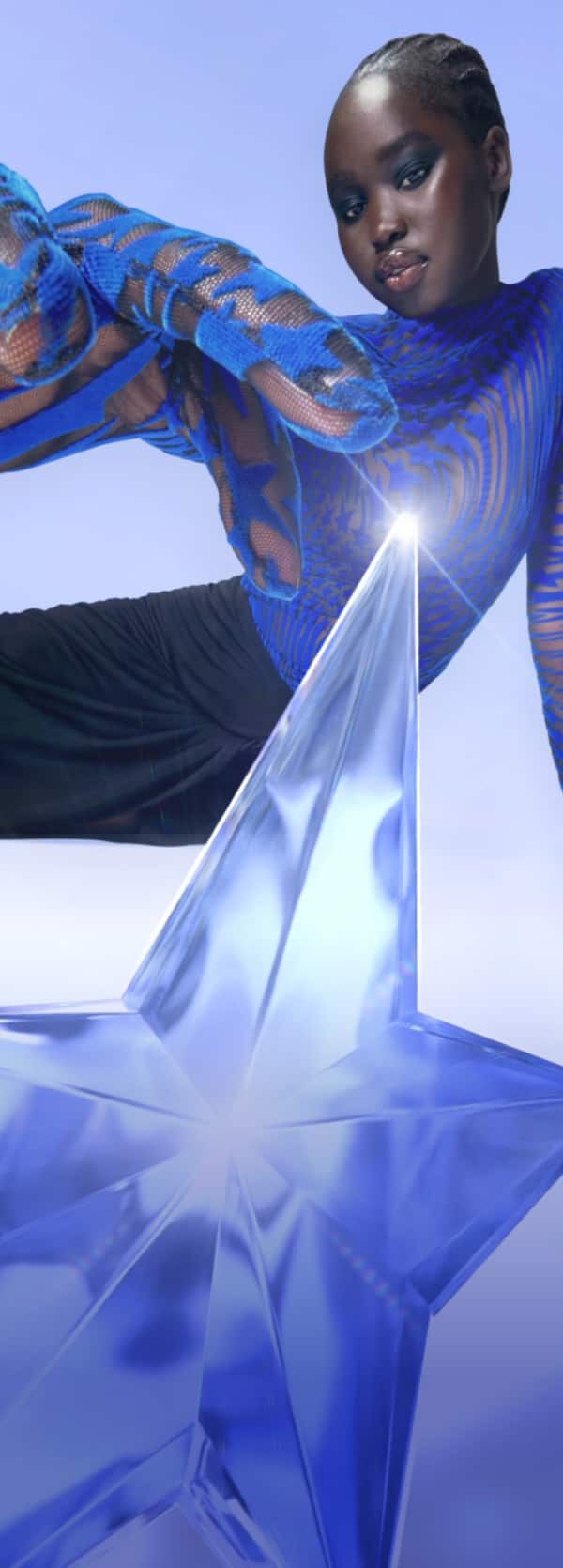 Une femme avec un haut bleu vibrant pose elegamment aux cotes d'une etoile en cristal sous un fond pastel.