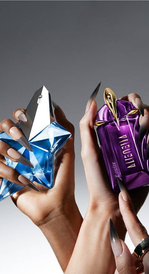 Deux mains tenant des flacons de parfum aux designs uniques, l'un en forme de diamant bleu et l'autre en forme de sac violet, sur un fond degrade.