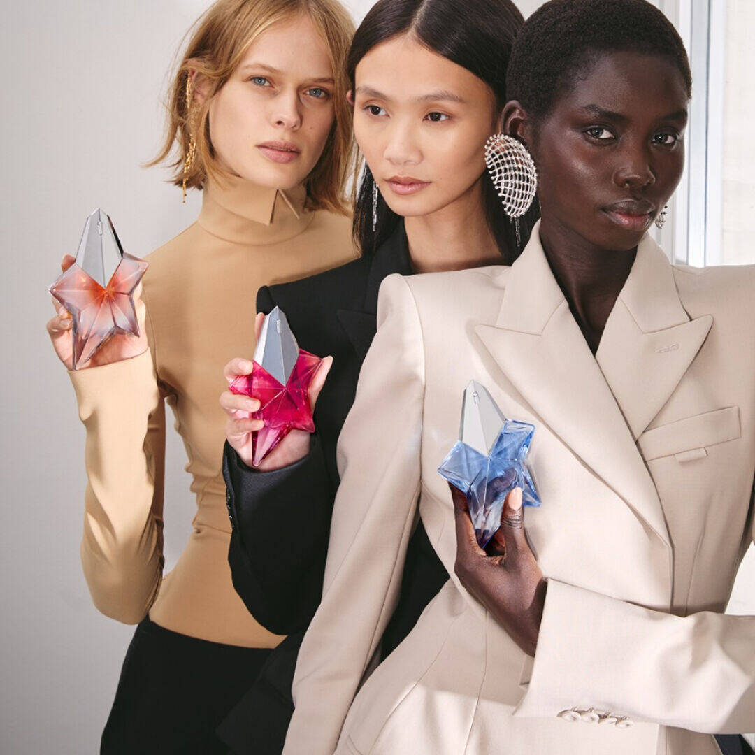 Trois mannequins vetus de noir et de beige tenant des flacons de parfum Mugler Angel en forme d'etoile, de couleur rose et bleue