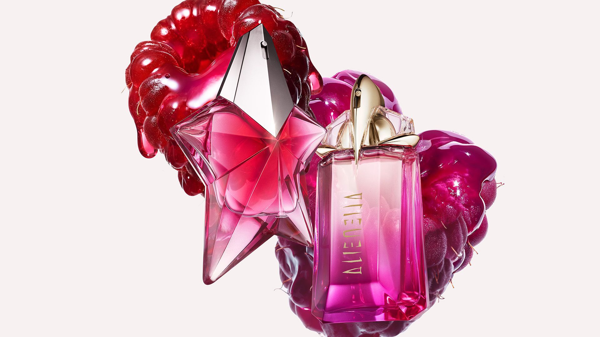deux flacons de parfums rose mugler devant deux framboises sur un fond clair