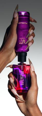 Main dans la main, deux flacons de parfum Mugler, l’un violet, l’autre rouge, sont en train d'etre assembles.