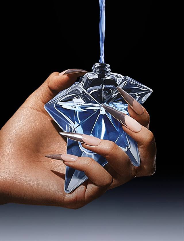 Main tenant un flacon de parfum en forme de diamant avec un liquide bleu a l'interieur, sur fond noir.