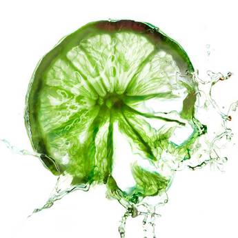 Tranche de lime verte avec des gouttes d'eau, sur fond lumineux.