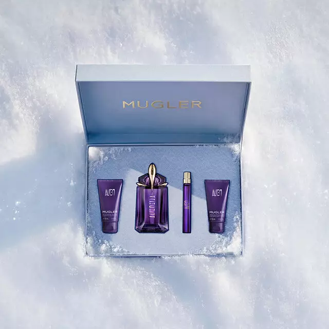 Un coffret cadeau Mugler bleu glacier, ouvert, texture et scintillant, pose sur de la neige, devoilant une lotion pour le corps « Alien », un gel douche, une eau de parfum de 60 ml ainsi qu'un format voyage de 10 ml. Le texte indique : « coffrets cadeaux inoubliables ».