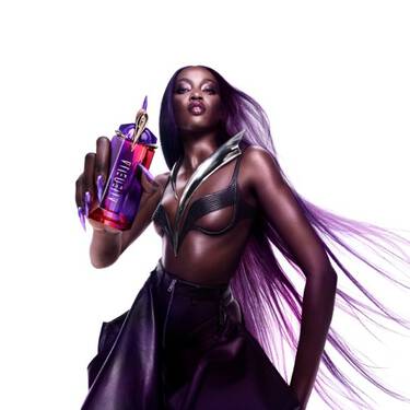 Une femme aux longs cheveux violets, vetue d'un soutien-gorge et d'une jupe noirs, tenant un flacon de parfum rouge et violet, sur fond blanc