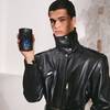 un homme habille d'une veste en cuir qui tient un flacon de parfum noir avec une etoile dans sa main