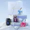 A stack of three light blue Mugler gift sets piled above the snow surrounded by a black A*Men eau de toilette bottle, a purple Alien eau de parfum bottle, a blue Angel eau de parfum bottle, and a pink Angel eau de parfum bottle in a snowy landscape.