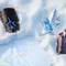 A black A*Men eau de toilette bottle, a blue star-shaped Angel eau de parfum bottle, and a purple Alien eau de parfum bottle lie together in the snow next to a glistening holiday gift set.