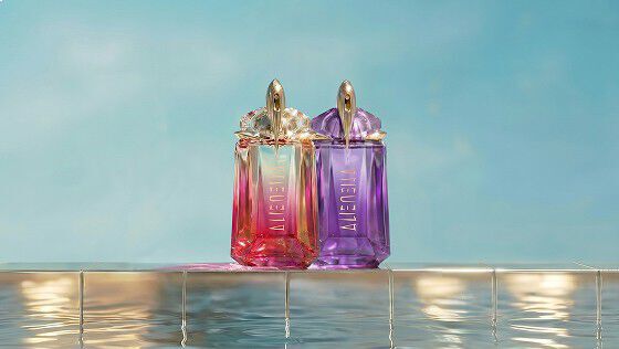 Mugler Alien Eau de Parfum and Alien Pulp bottles in violet and pink stand side by side on a tiled pool edge with water reflections and a soft blue backdrop.