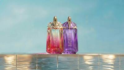 Mugler Alien Eau de Parfum and Alien Pulp bottles in violet and pink stand side by side on a tiled pool edge with water reflections and a soft blue backdrop.
