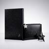 un bloc note noir, une trousse noir mugler et une etoile noir sur un fond gris clair