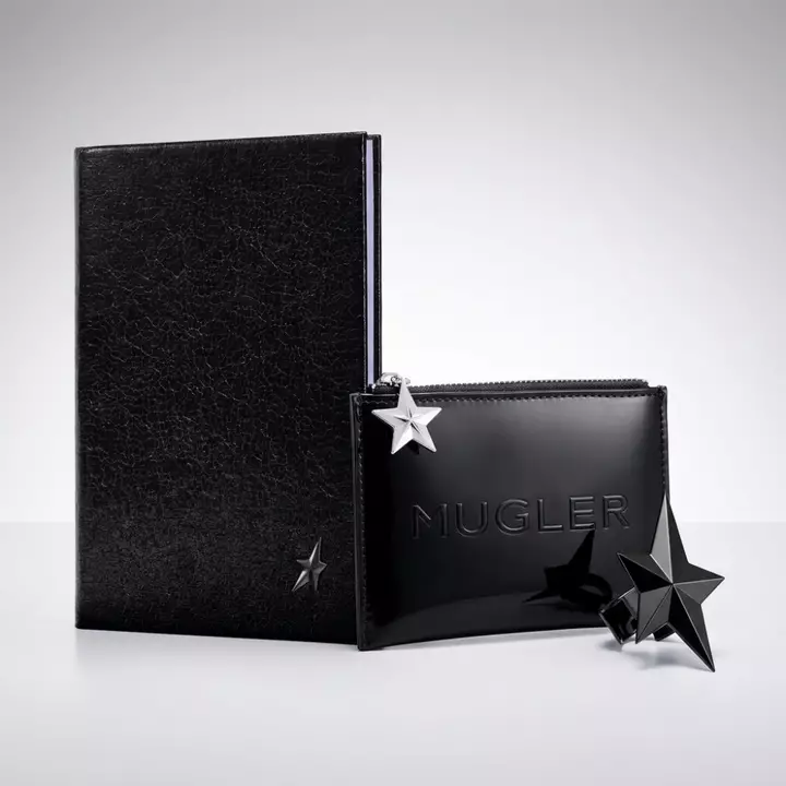 un bloc note noir, une trousse noir mugler et une etoile noir sur un fond gris clair