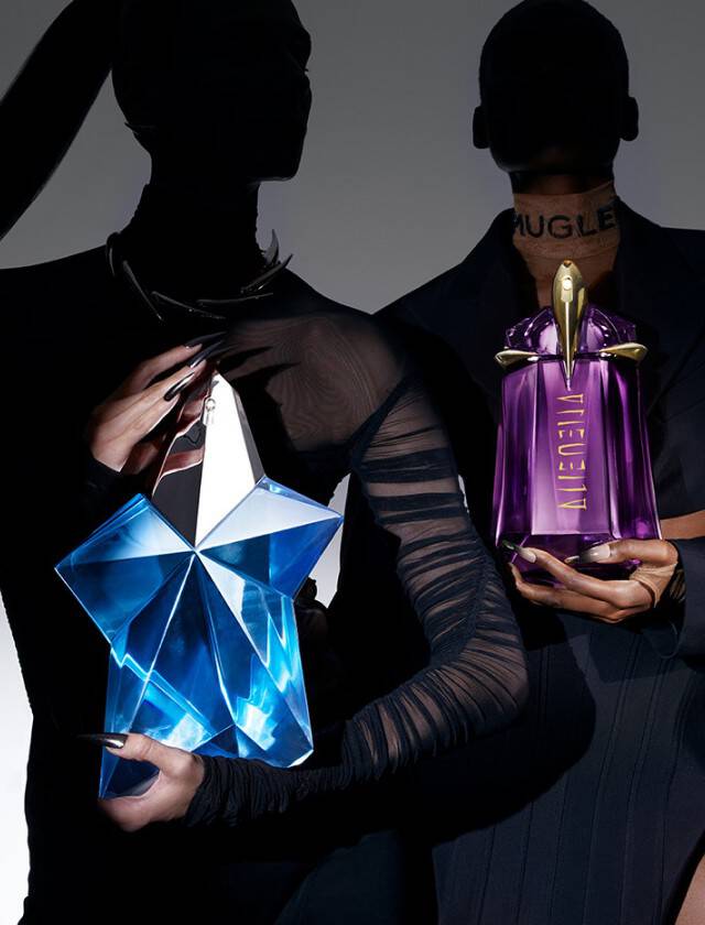 Deux silhouettes de femmes tiennent chacune un flacon de parfum, l'une avec un flacon bleu et l'autre avec un flacon violet, sur fond sombre.
