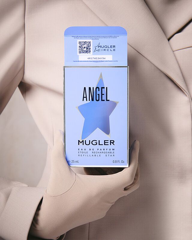 Une personne vetue d'un blazer et de gants beige clair, tenant une boite de parfum bleu clair avec une decoupe en forme d'etoile et du texte noir.