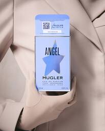 Une personne vetue d'un blazer et de gants beige clair, tenant une boite de parfum bleu clair avec une decoupe en forme d'etoile et du texte noir.