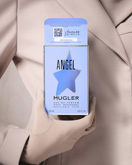 Une personne vetue d'un blazer et de gants beige clair, tenant une boite de parfum bleu clair avec une decoupe en forme d'etoile et du texte noir.