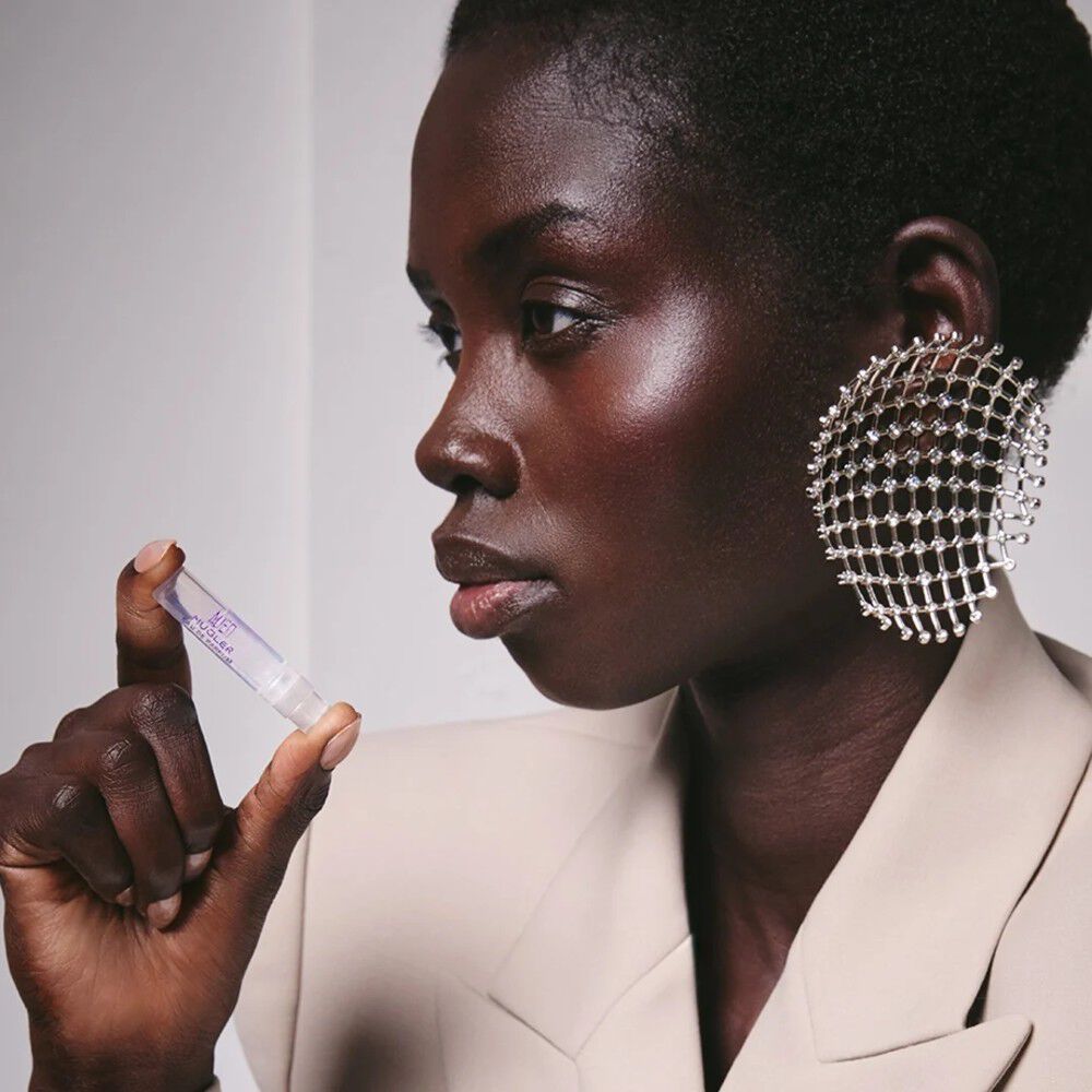 profil d'une femme aux cheveux courts tenant un echantillon de parfum Mugler dans la main