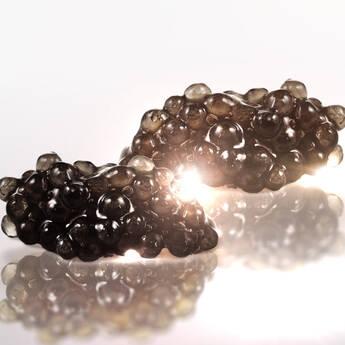 Deux morceaux de caviar noir brillants, poses sur une surface reflechissante, avec des reflets lumineux.
