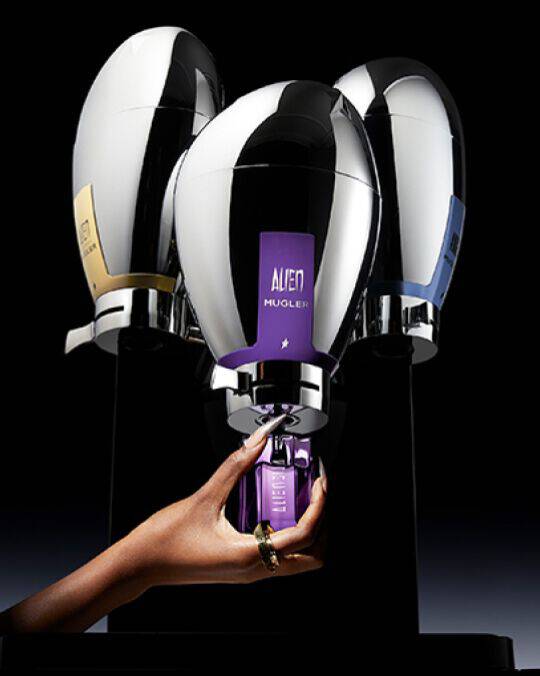trois fontaines de parfums mugler avec au milieu une main tenant un flacon violet alien a recharger