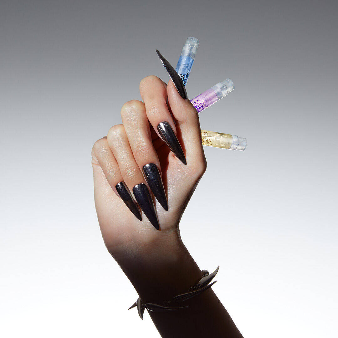 Main avec des ongles longs et pointus, tenant plusieurs flacons de parfum.