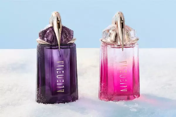 Deux flacons de parfum Mugler Alien — l'un d'un violet fonce classique (Alien eau de parfum) et l'autre d'un rose vif (Alien pulp) — poses cote a cote sur une table de banquet recouverte de neige.