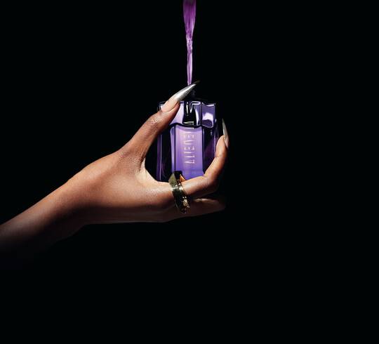 un flacon de parfum violet alien tenue dans une main qui est rempli par du parfum