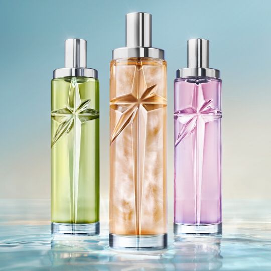 trois flacons de parfums rose, vert et orange poses sur de l'eau.