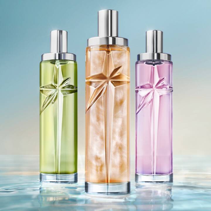 trois flacons de parfums rose, vert et orange poses sur de l'eau.