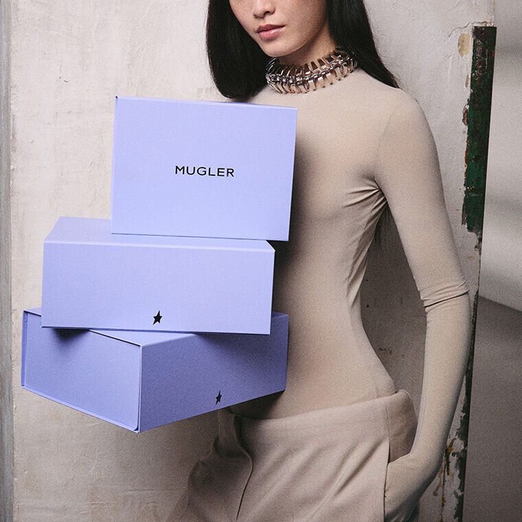 une femme habille en beige  portant trois boites cadeaux bleus mugler