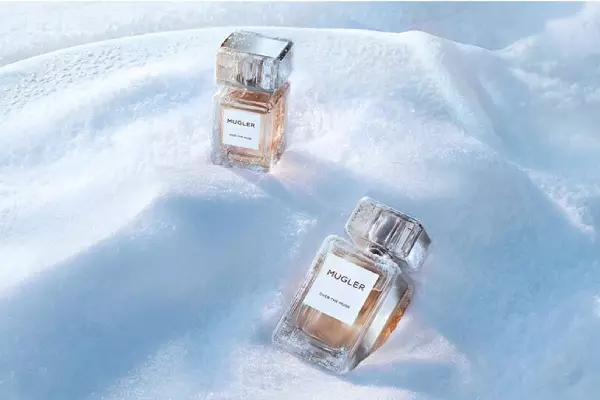 Deux flacons de parfum Mugler « Les Exceptions », elegants, carres et en verre epais, remplis d'un liquide dore, poses en desequilibre dans un paysage enneige.