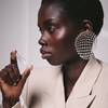 une femme a al peau noire habille en beige qui tient un echantillon de parfum