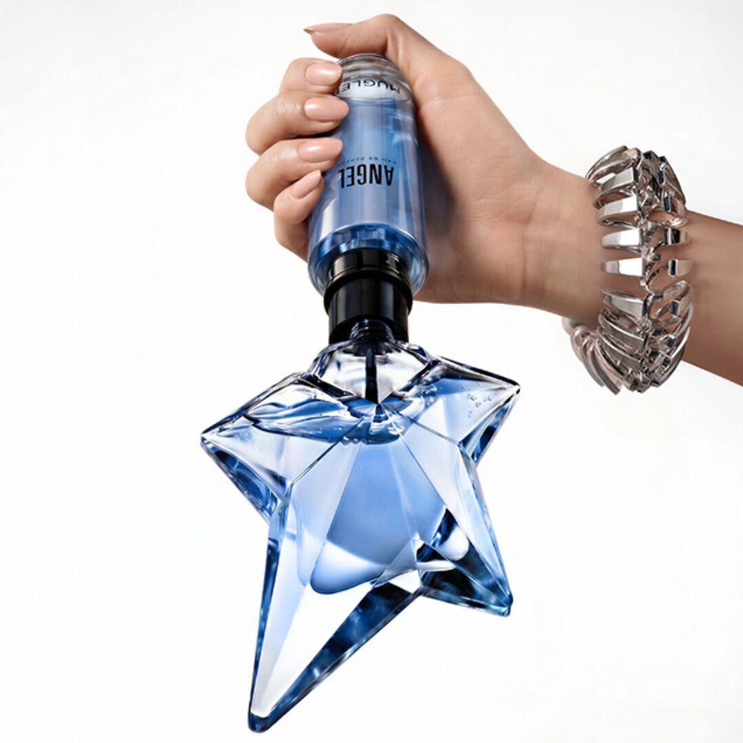 un flacon de parfum en forme d'etoile bleu avec une main qui tient un flacon recharge