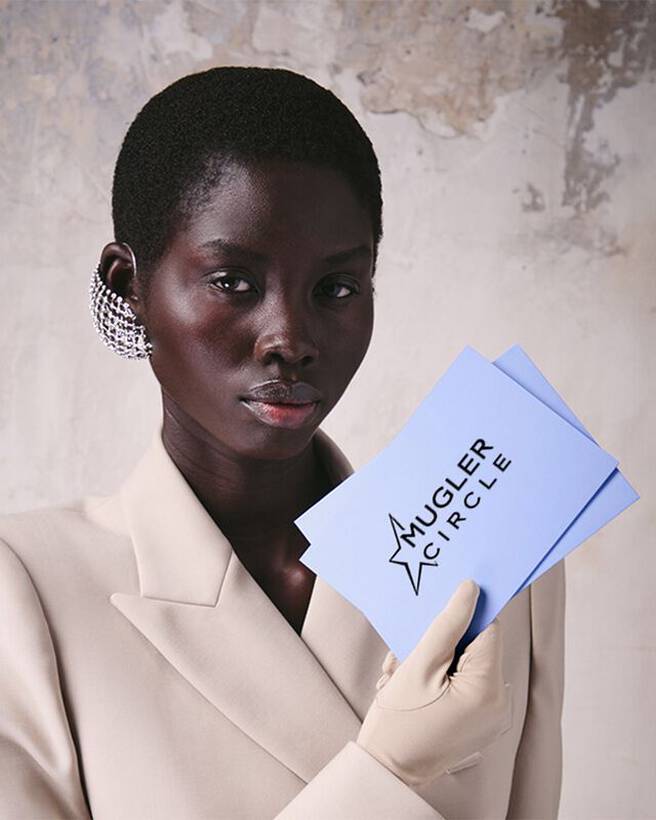 Gros plan sur un mannequin tenant des cartes bleu clair du programme de fidelite « Mugler Circle ».