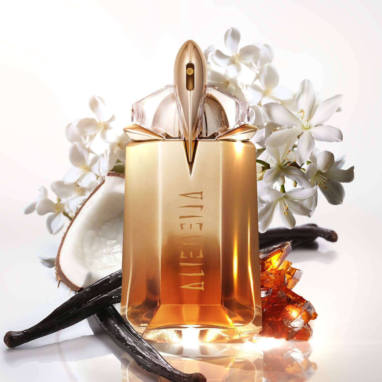 Flacon de parfum dore sur un fond de fleurs blanches et de noix de coco, avec des eclats d'ambre et des gousses de vanille.