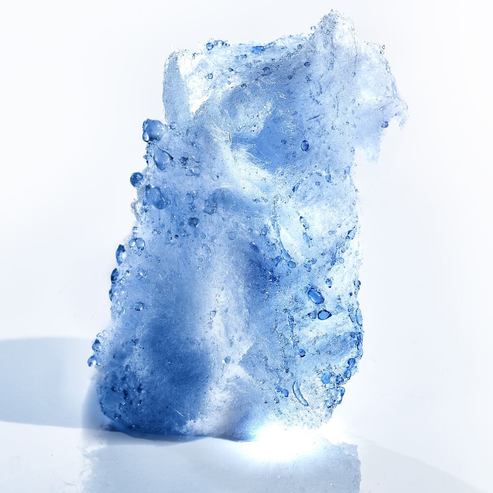 Un morceau de glace transparente, illumine, avec des gouttes d'eau sur sa surface, pose sur un fond clair.