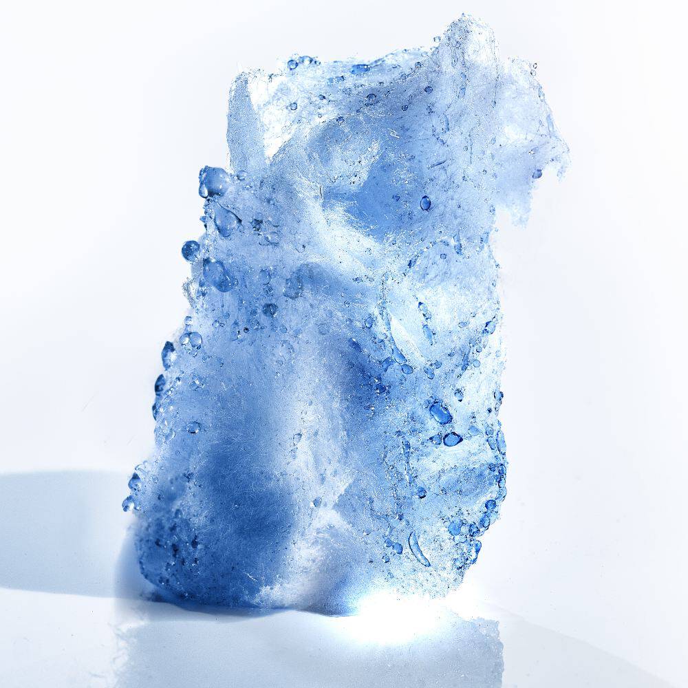 Un morceau de glace transparente, illumine, avec des gouttes d'eau sur sa surface, pose sur un fond clair.